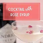 Pale pink cocktail in a coupe glass with rose petals floating on top, with a gin bottle blurred in the background