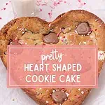 Heart shaped chocolate chip cookie cake with chocolate hearts and pink sprinkles on parchment paper