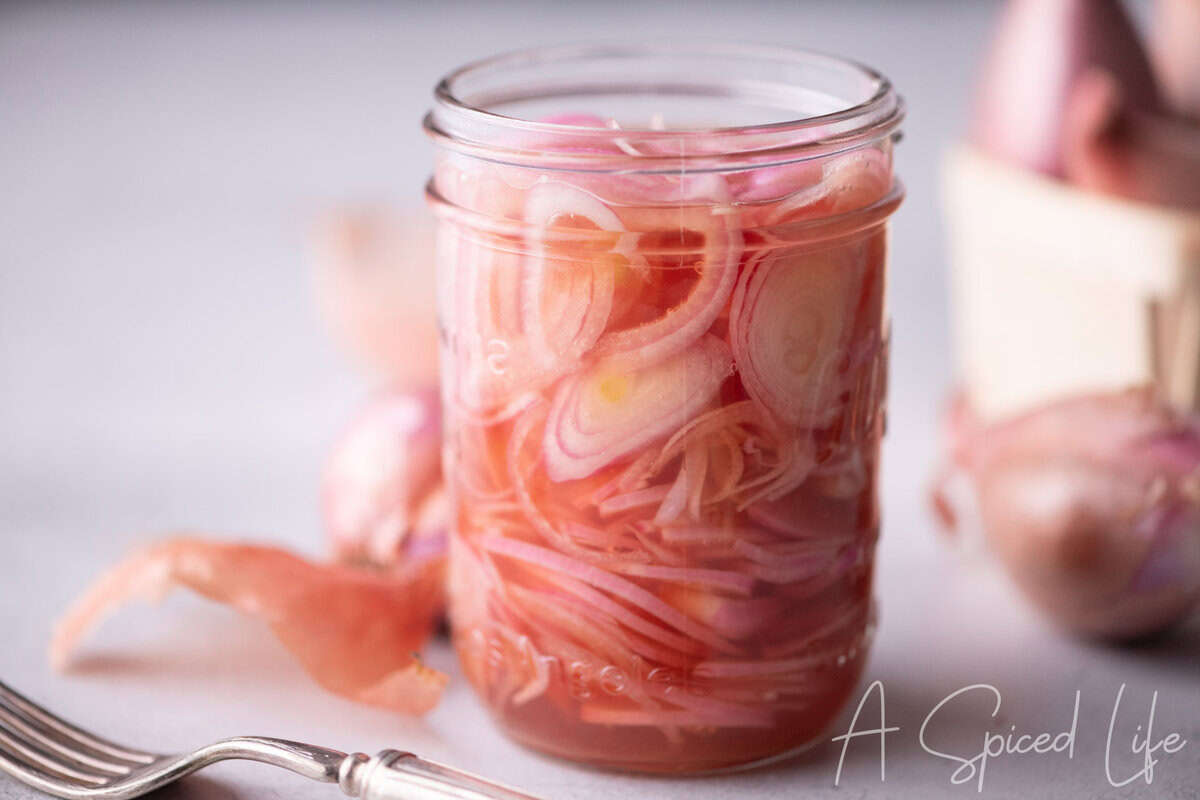 Glass jar filled with thinly sliced shallots in a pink pickling liquid