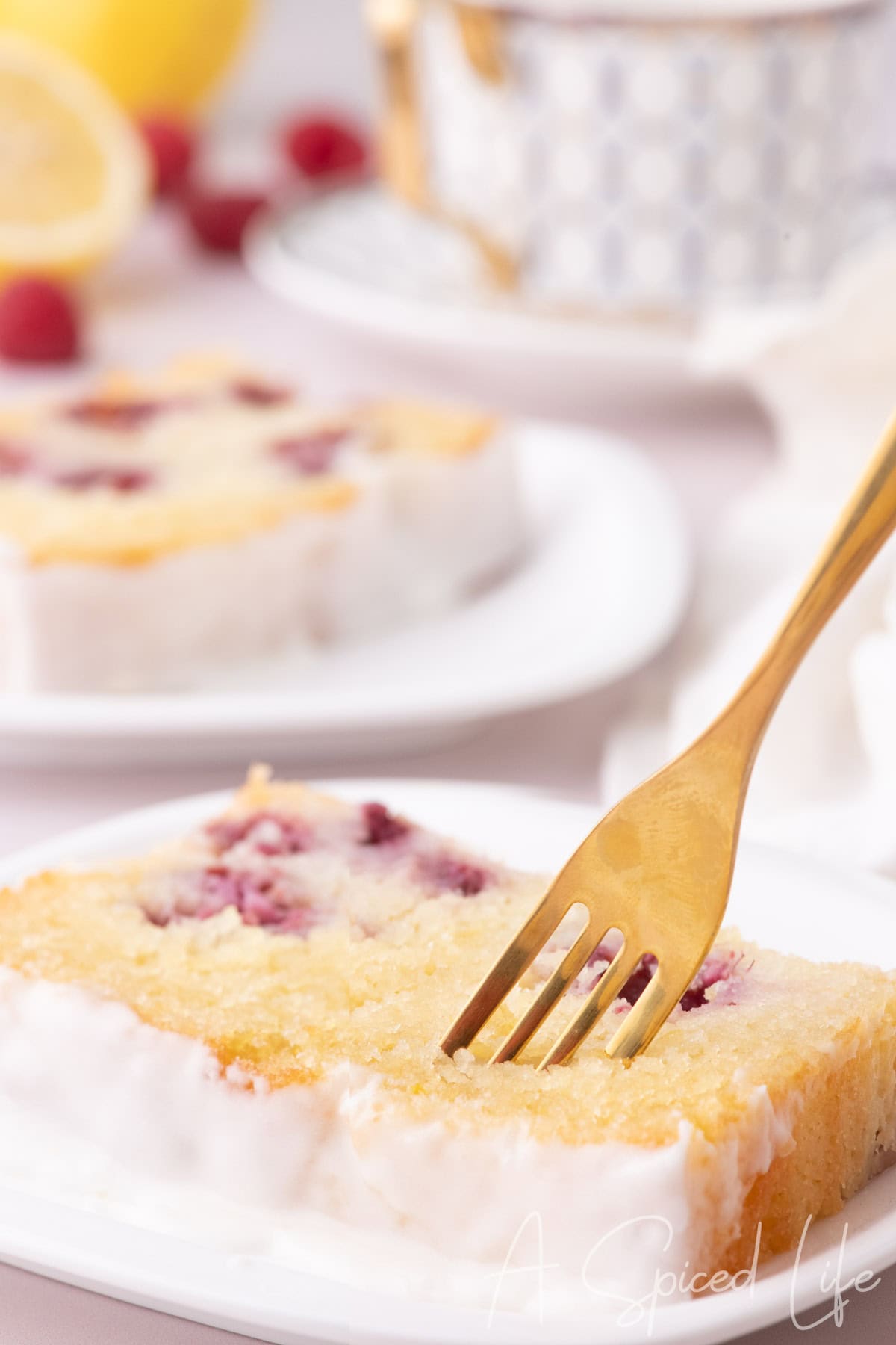 Fork cutting into a glazed slice of raspberry lemon loaf on a white plate