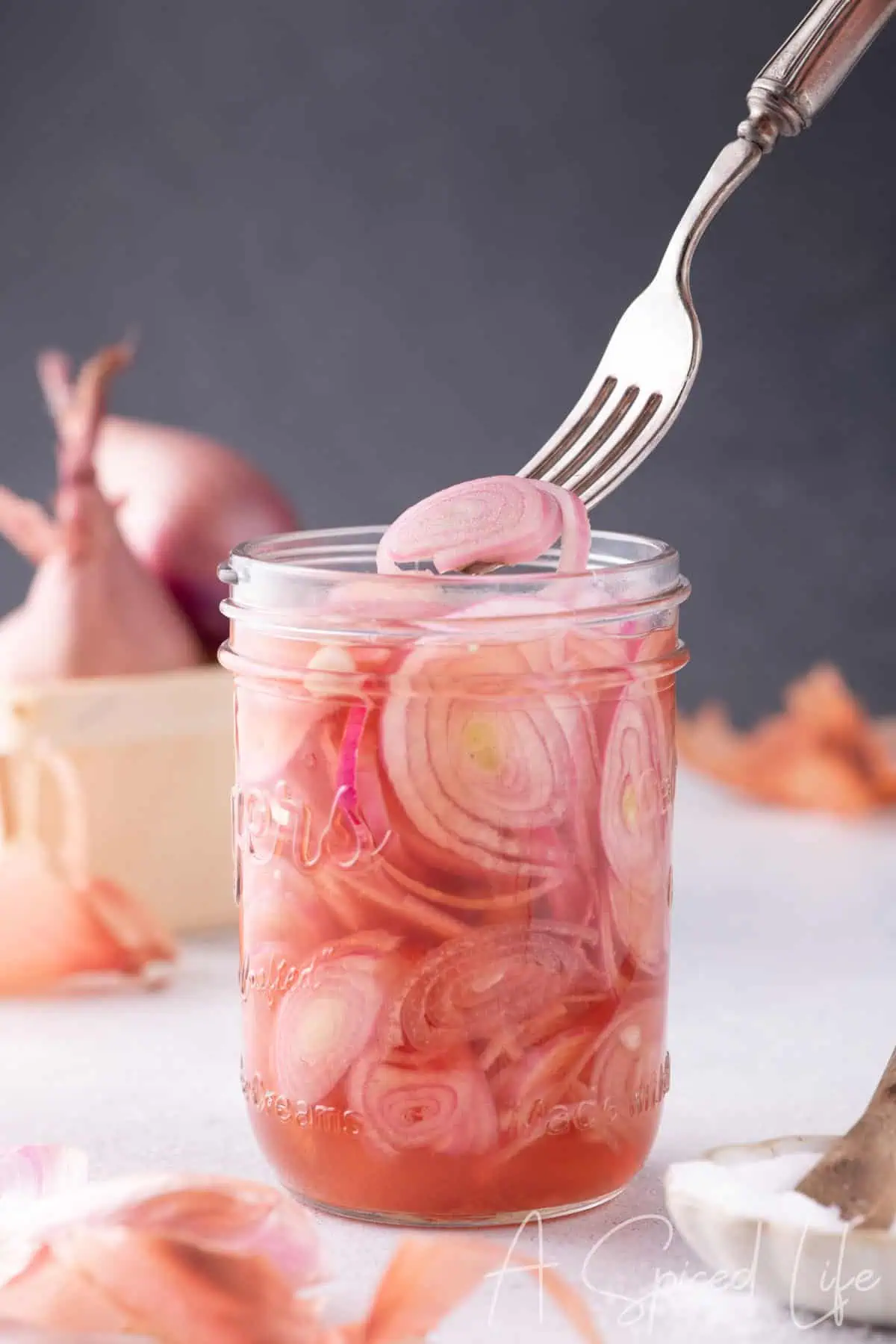 Fork lifting thinly sliced quick pickled shallots from a jar with pink vinegar brine