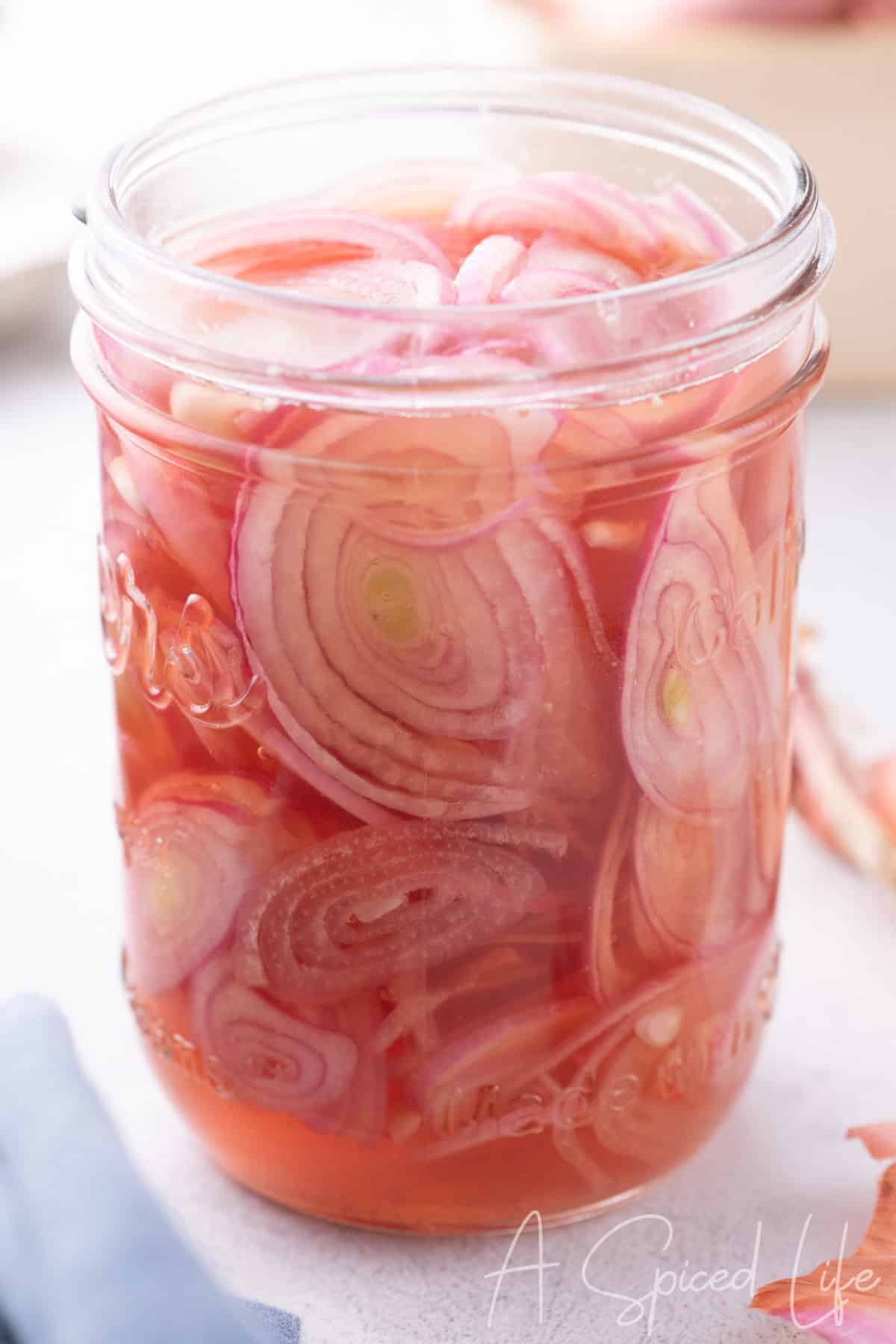 Close-up of jar filled with thinly sliced pickled shallots in pink vinegar brine