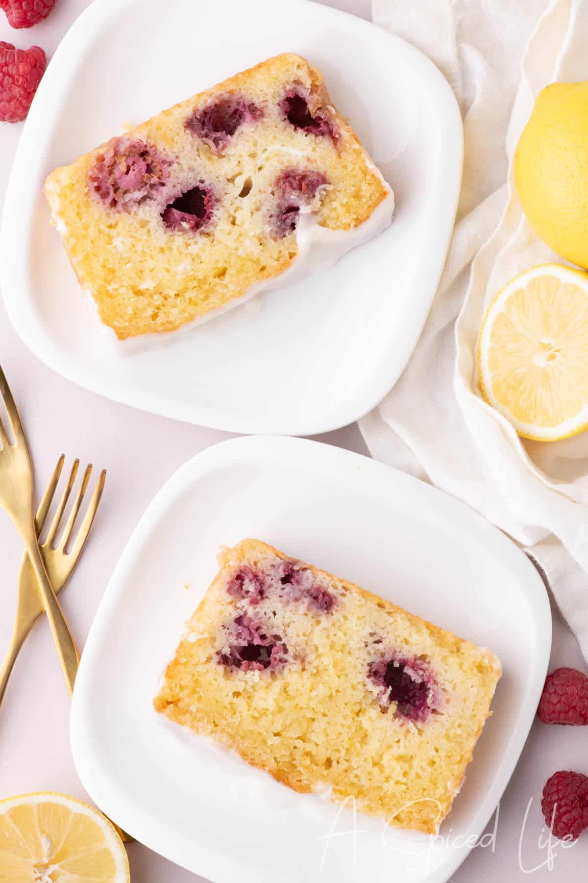 Two slices of glazed raspberry lemon loaf served on white plates with lemon slices