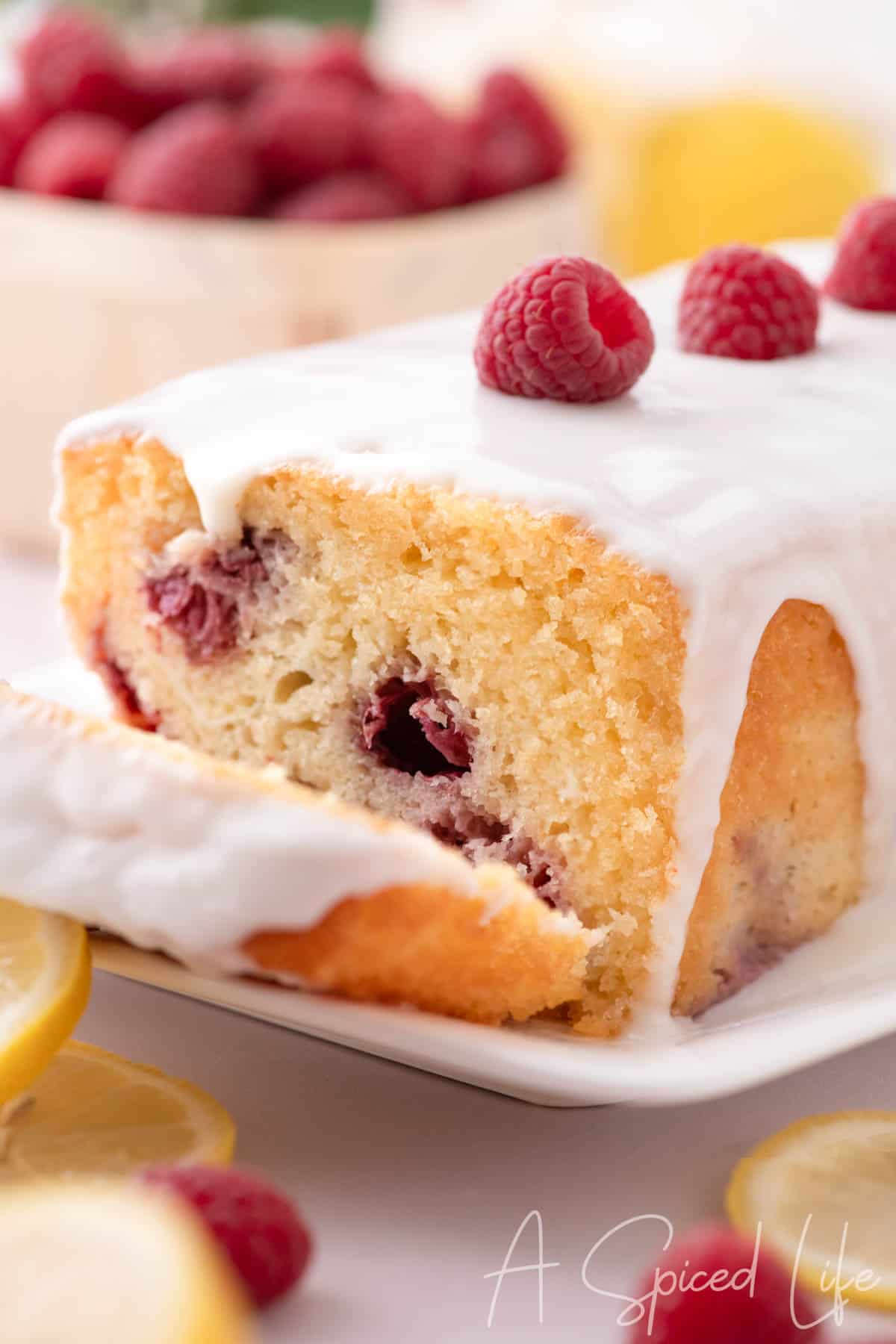Lemon raspberry cake with glaze and fresh raspberries on top, sliced to show crumb
