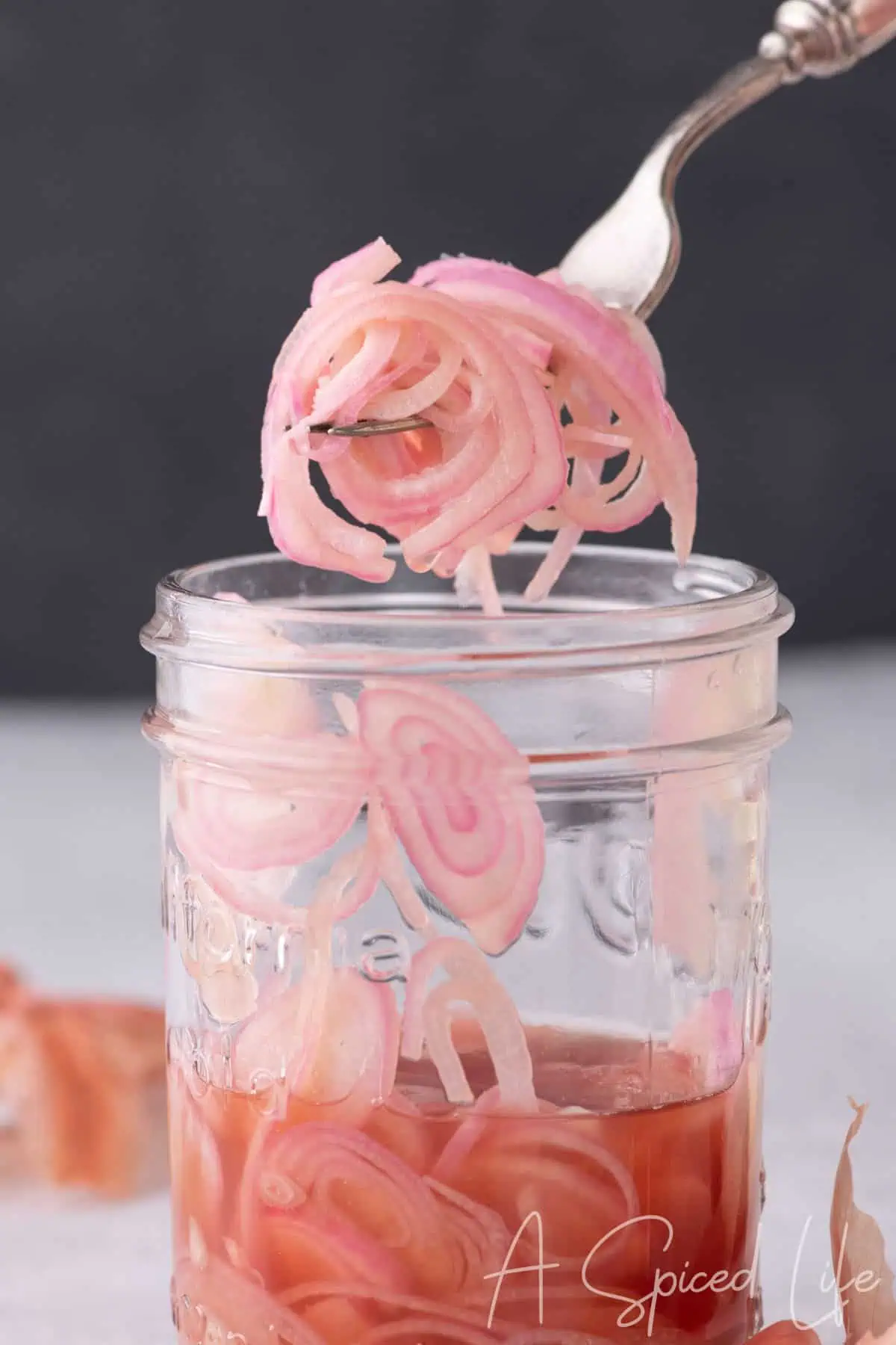 Fork lifting delicate strands of quick pickled shallots from a glass jar with pink brine