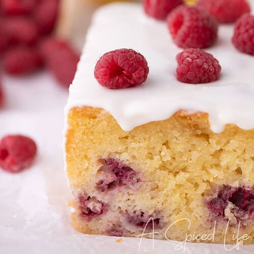 Slice of raspberry lemon loaf cake with lemon glaze and fresh raspberries on top