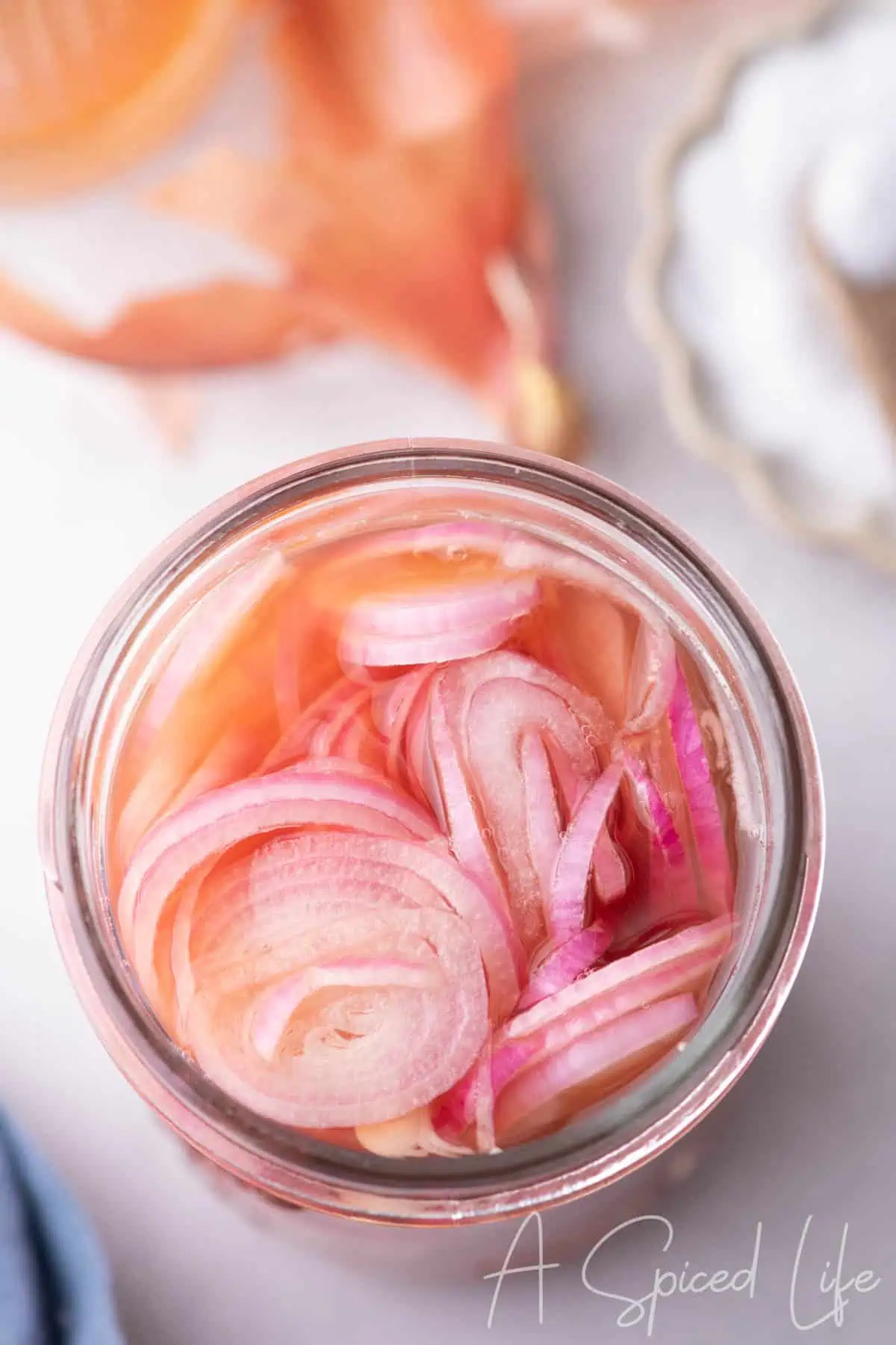 Overhead view of quick pickled shallots in a glass jar with pink brine
