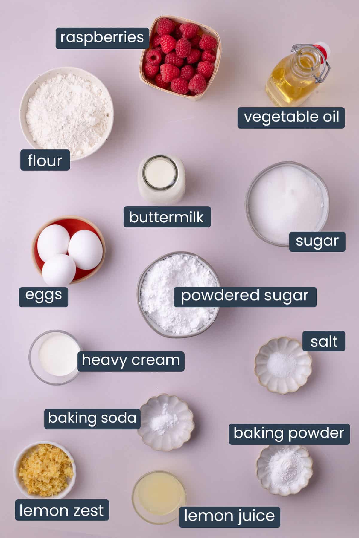Flat lay of ingredients for raspberry lemon loaf including raspberries, flour, eggs, sugar, buttermilk, and lemon zest