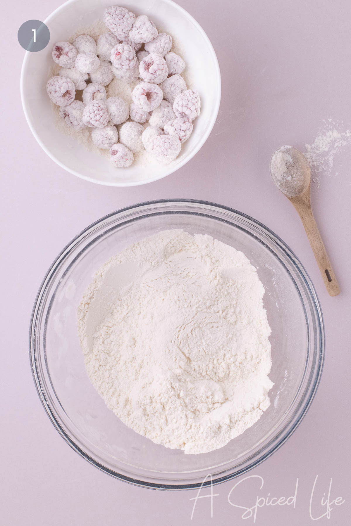 Fresh raspberries coated in flour beside a bowl of dry ingredients for the loaf