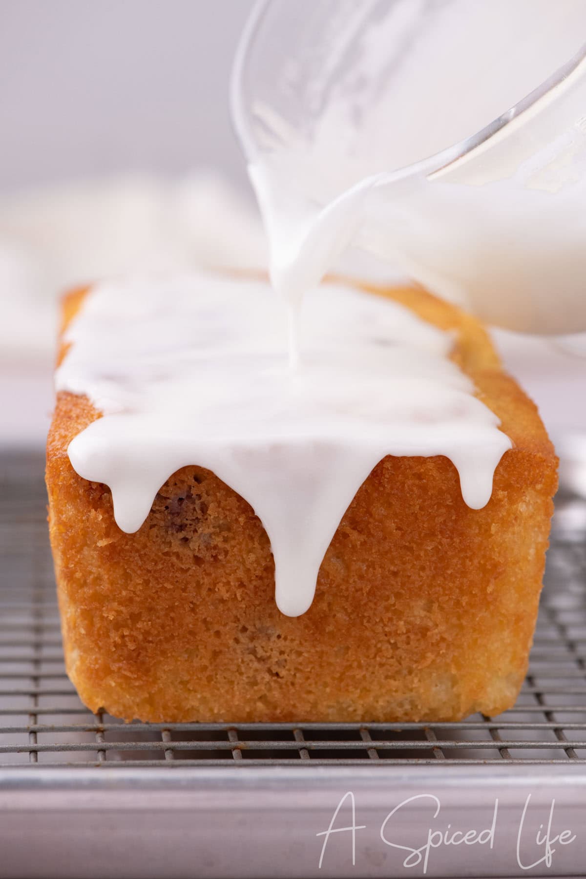 Glaze being poured over raspberry lemon loaf on a cooling rack