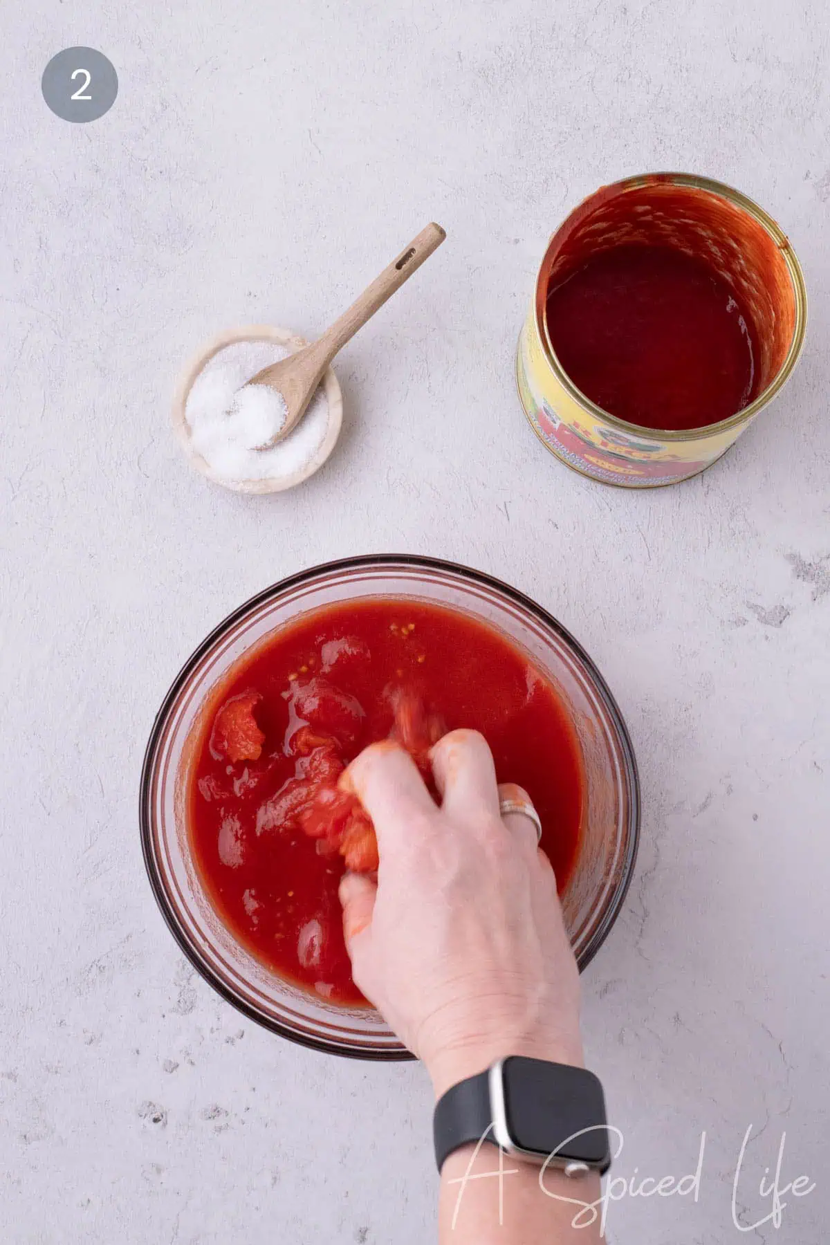 Hand crushing whole tomatoes in a bowl to create rustic pizza sauce