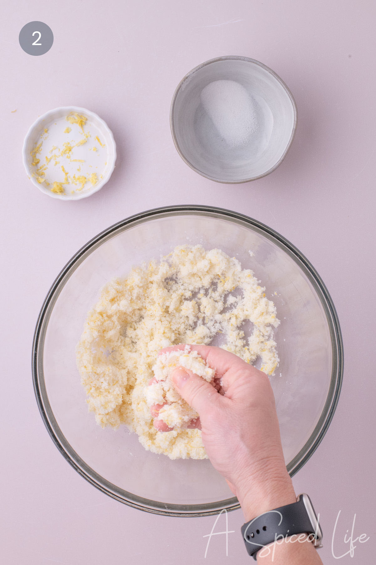 Hand rubbing lemon zest into granulated sugar in a glass mixing bowl
