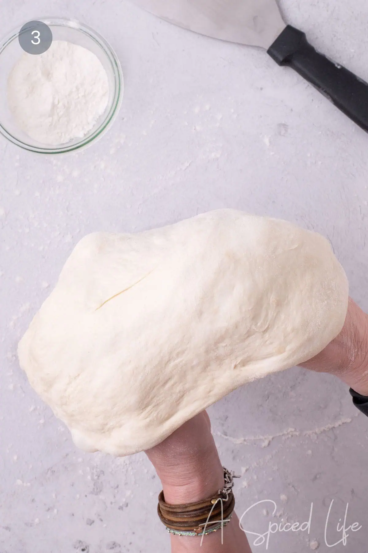 Stretching store-bought pizza dough by hand over knuckles to form thin pizza crust