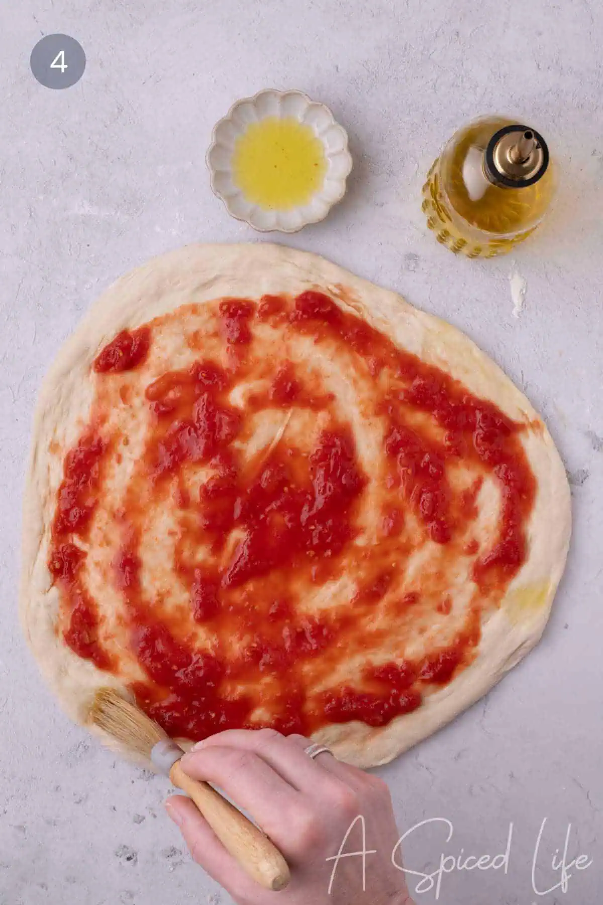Spreading crushed tomato sauce on stretched pizza dough with olive oil