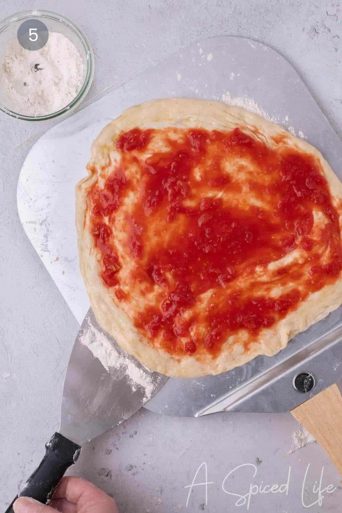 Raw pizza with tomato sauce resting on a floured pizza peel before baking