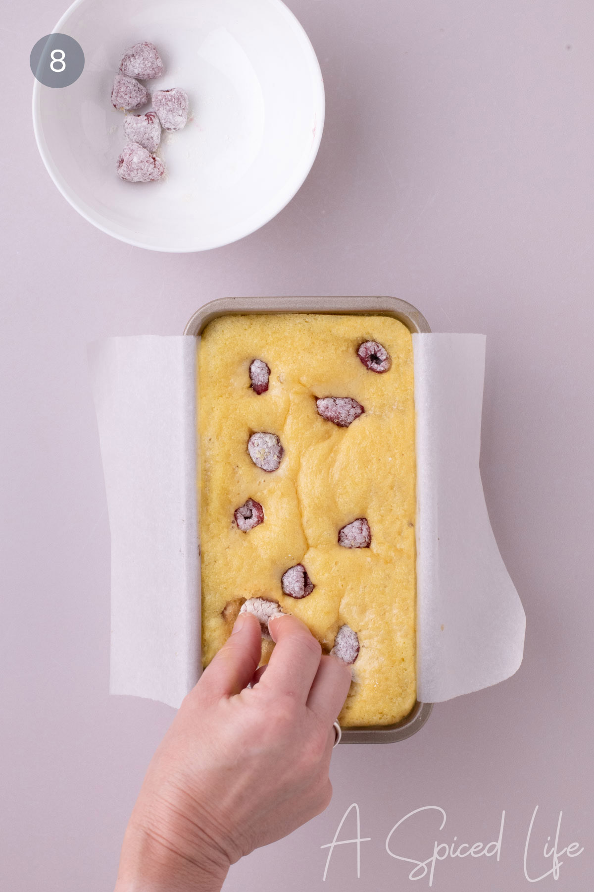 Reserved raspberries being added to the top of a partially baked loaf