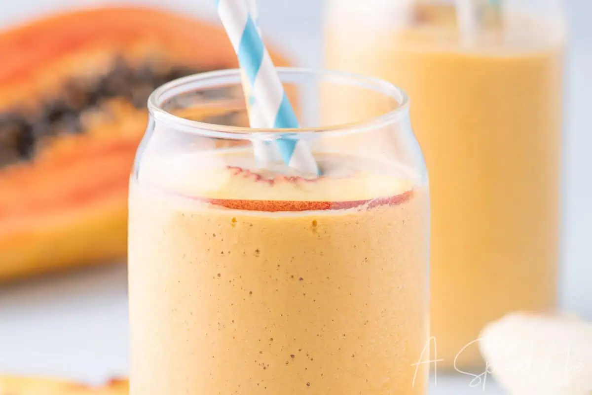 Close up of chilled tropical banana smoothie with papaya in background
