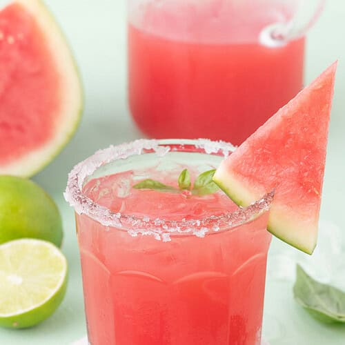 Basil watermelon margarita in a glass with a sugared rim, watermelon slice garnish, and fresh lime