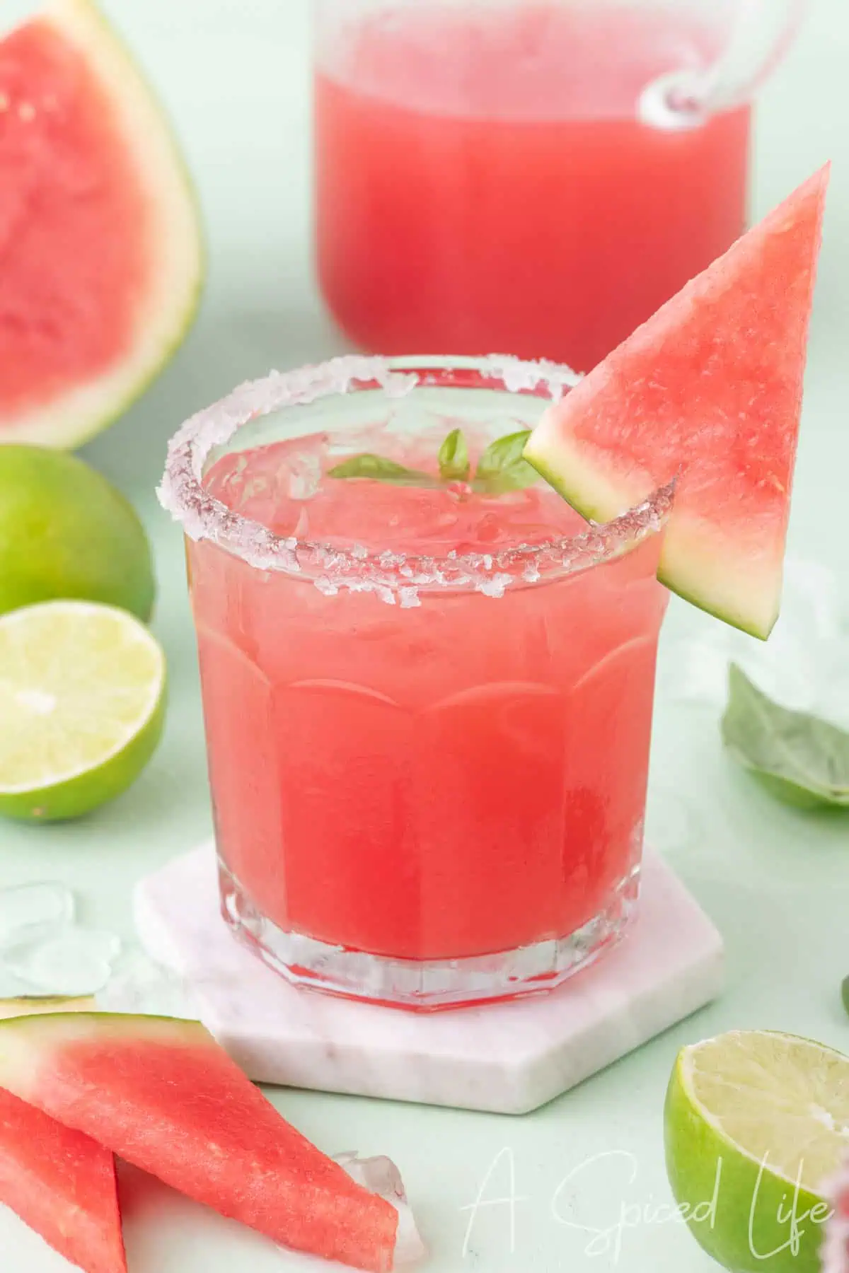 Basil watermelon margarita in a glass with a sugared rim, watermelon slice garnish, and fresh lime
