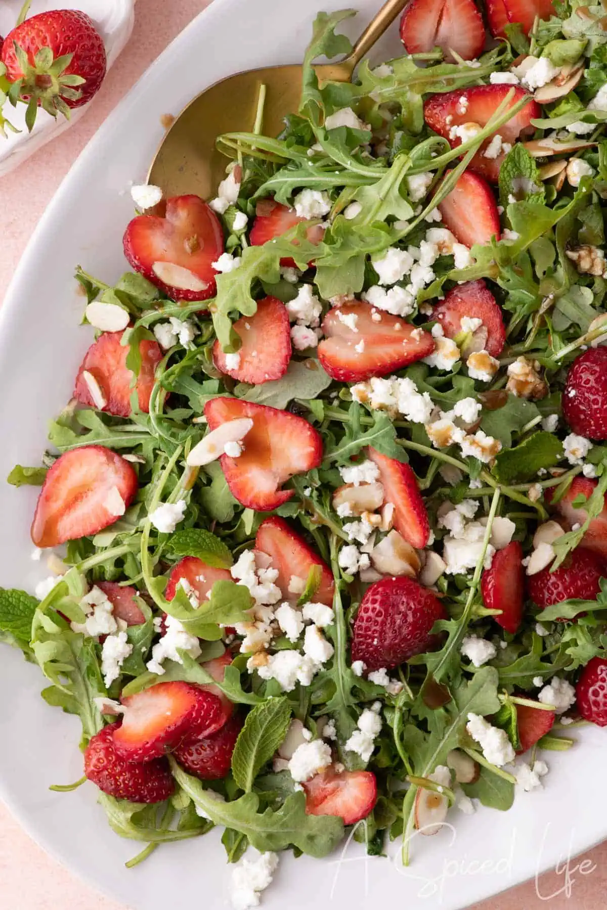 Overhead view of arugula salad with strawberries, crumbled goat cheese, and sliced almonds