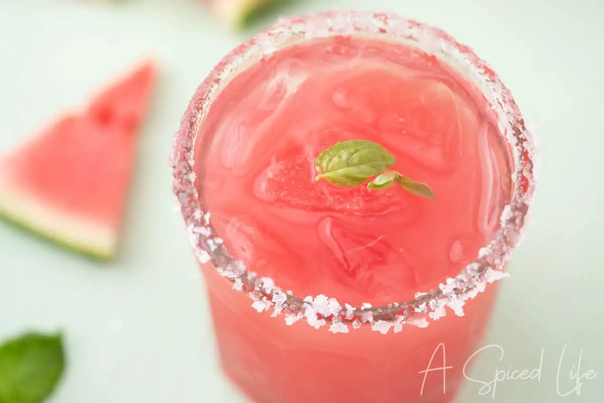 Close-up of a watermelon basil margarita with a sugared rim and fresh basil garnish