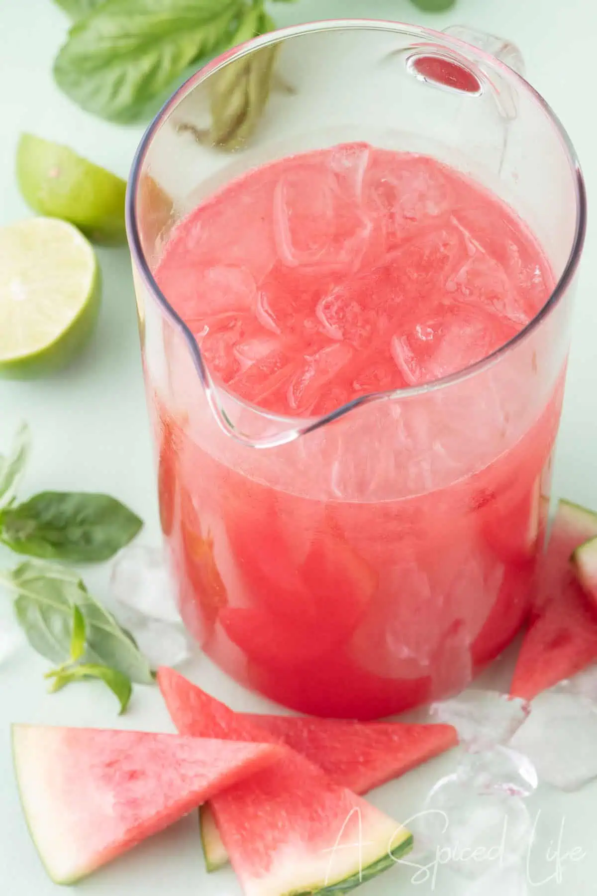 Pitcher of watermelon basil margarita with ice, fresh basil, lime, and watermelon slices