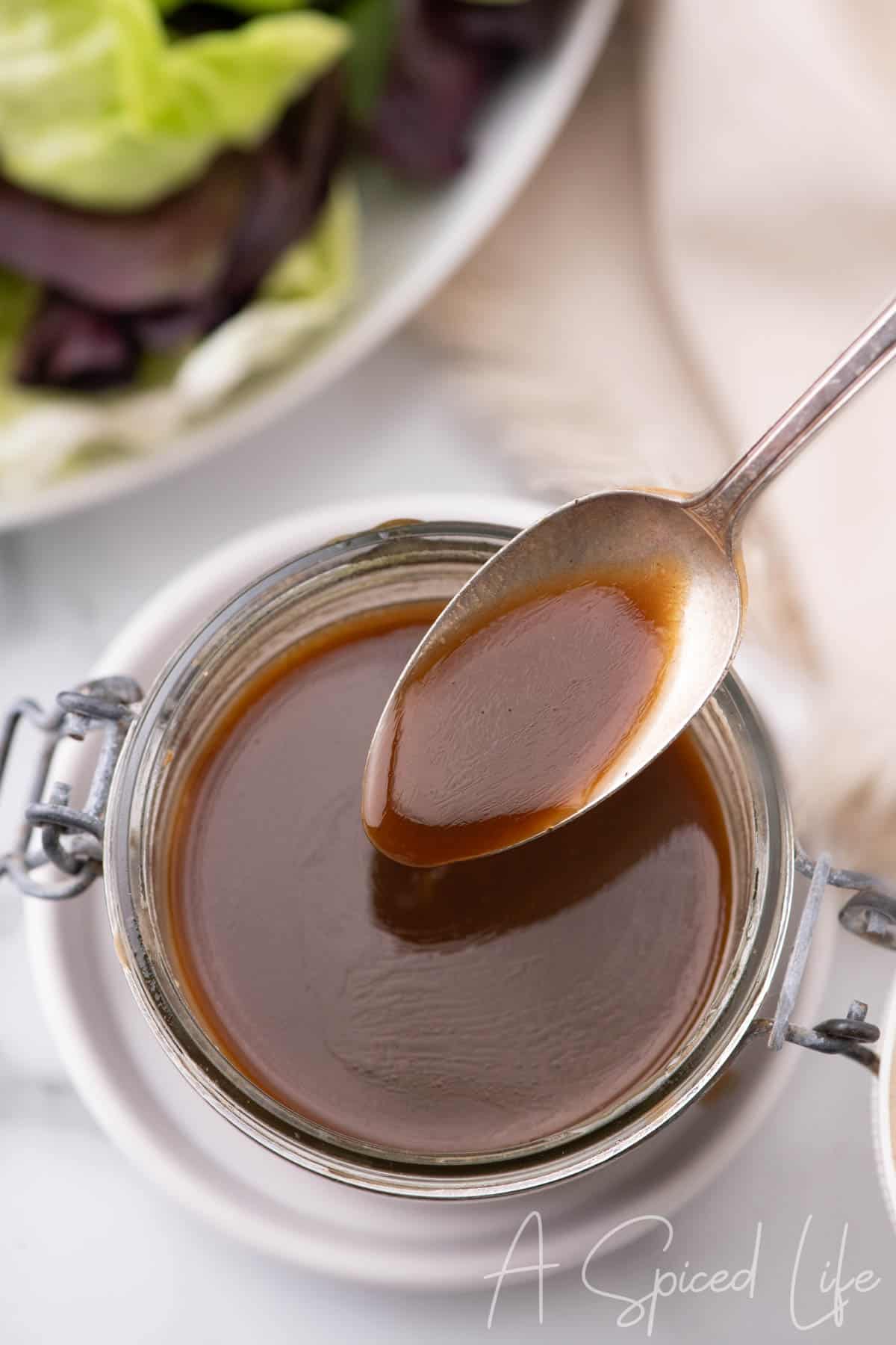 Spoon holding glossy balsamic and lemon dressing above a jar.