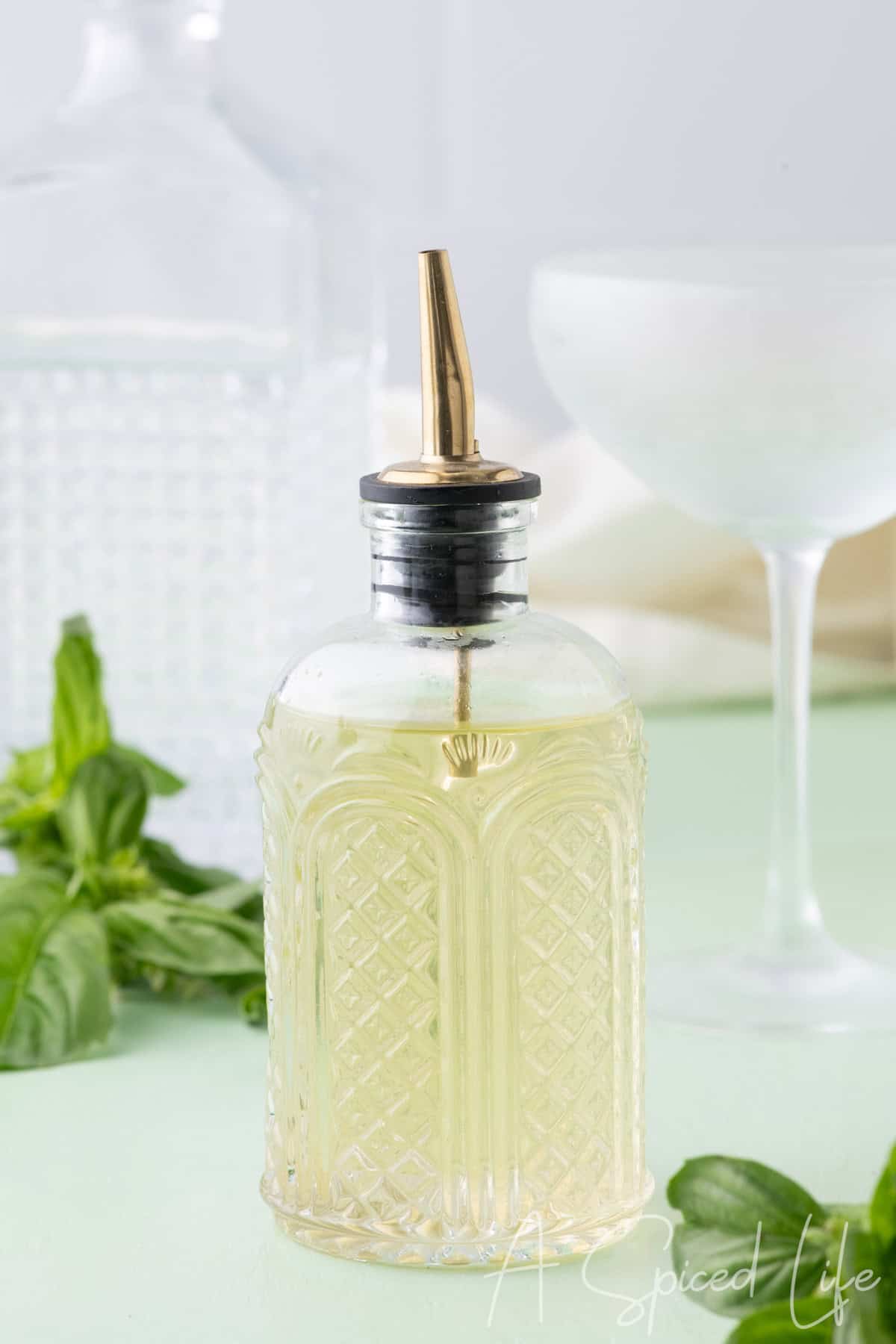 Homemade basil syrup in a glass bottle with fresh basil leaves and cocktail glass
