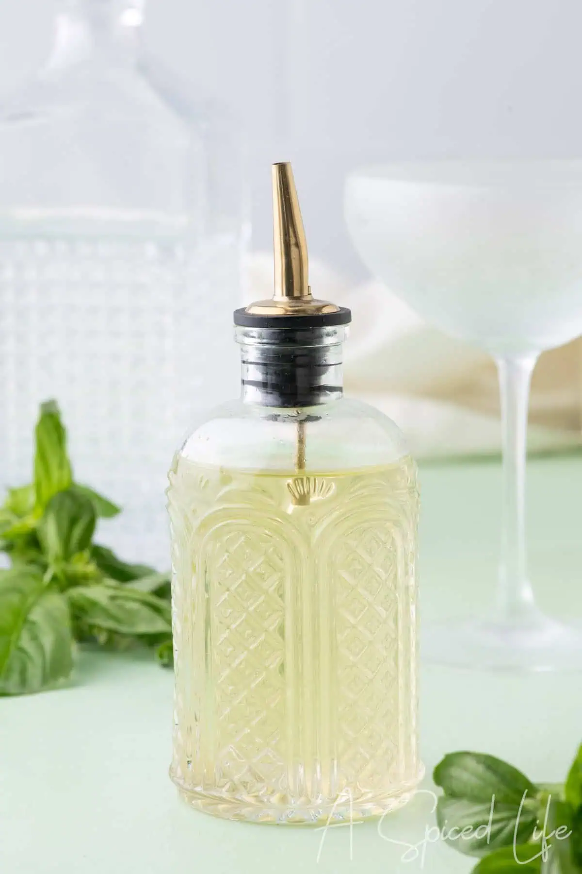Homemade basil syrup in a glass bottle with fresh basil leaves and cocktail glass