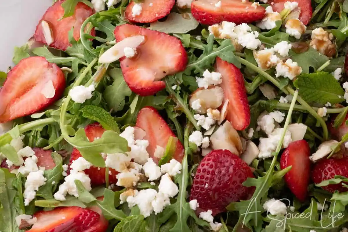 Styled strawberry arugula salad with goat cheese served on a platter with gold utensils