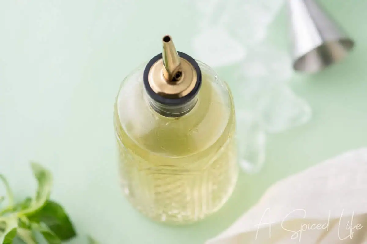 Overhead view of basil syrup in a glass bottle with ice and cocktail tools