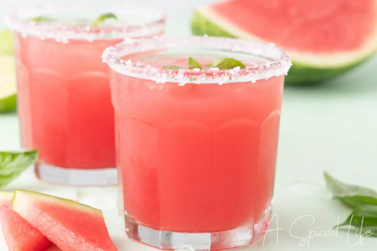 Two watermelon basil margaritas with sugared rims and fresh basil garnish