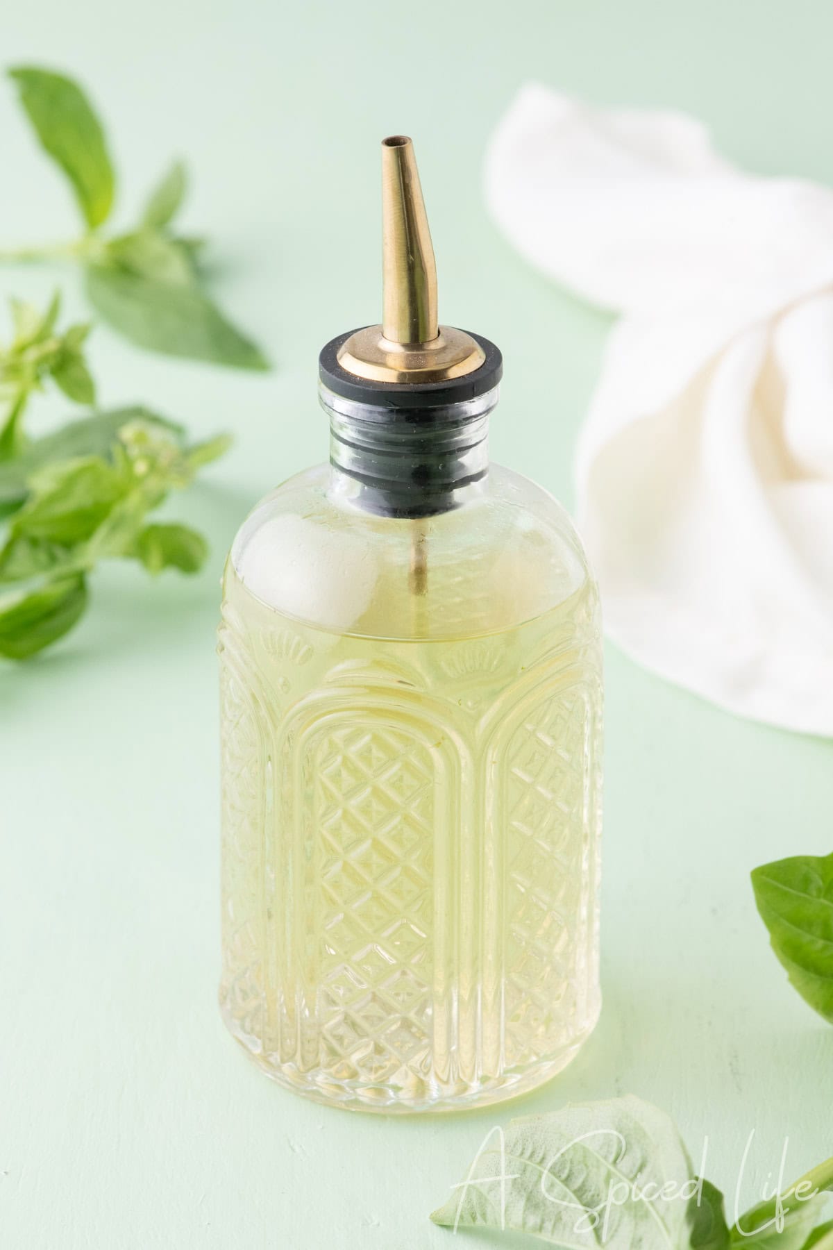 Homemade simple syrup infused with basil in a glass bottle with fresh basil leaves nearby