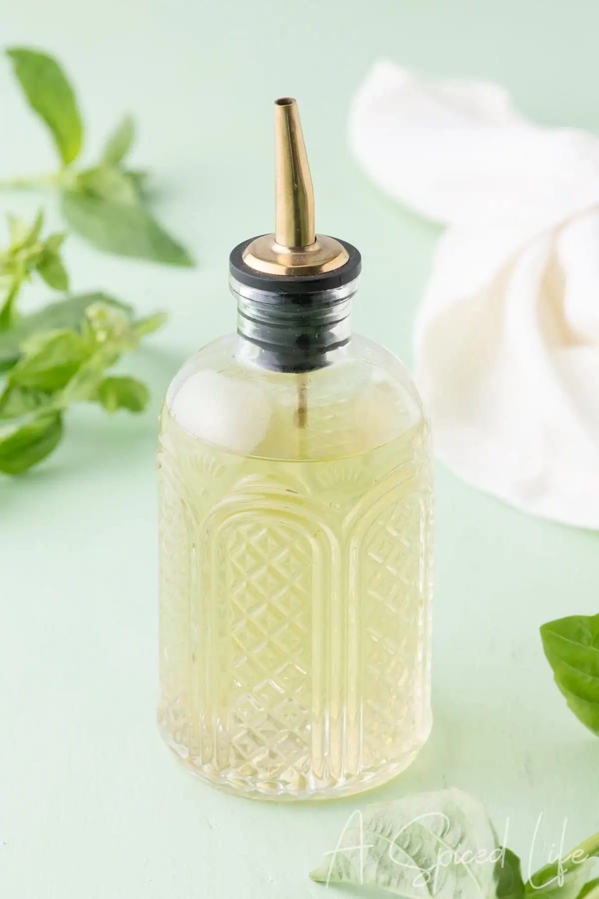 Homemade simple syrup infused with basil in a glass bottle with fresh basil leaves nearby