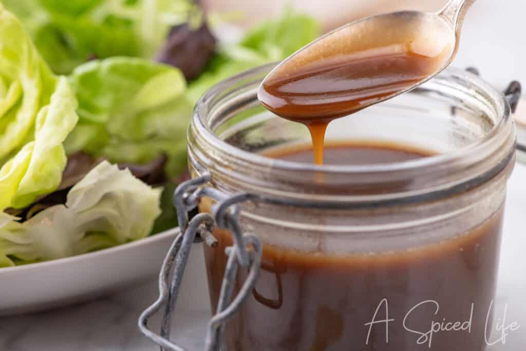 Spoon drizzling balsamic dressing from a jar with lettuce in the background.