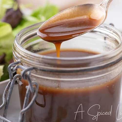 Spoon drizzling balsamic dressing from a jar with lettuce in the background.