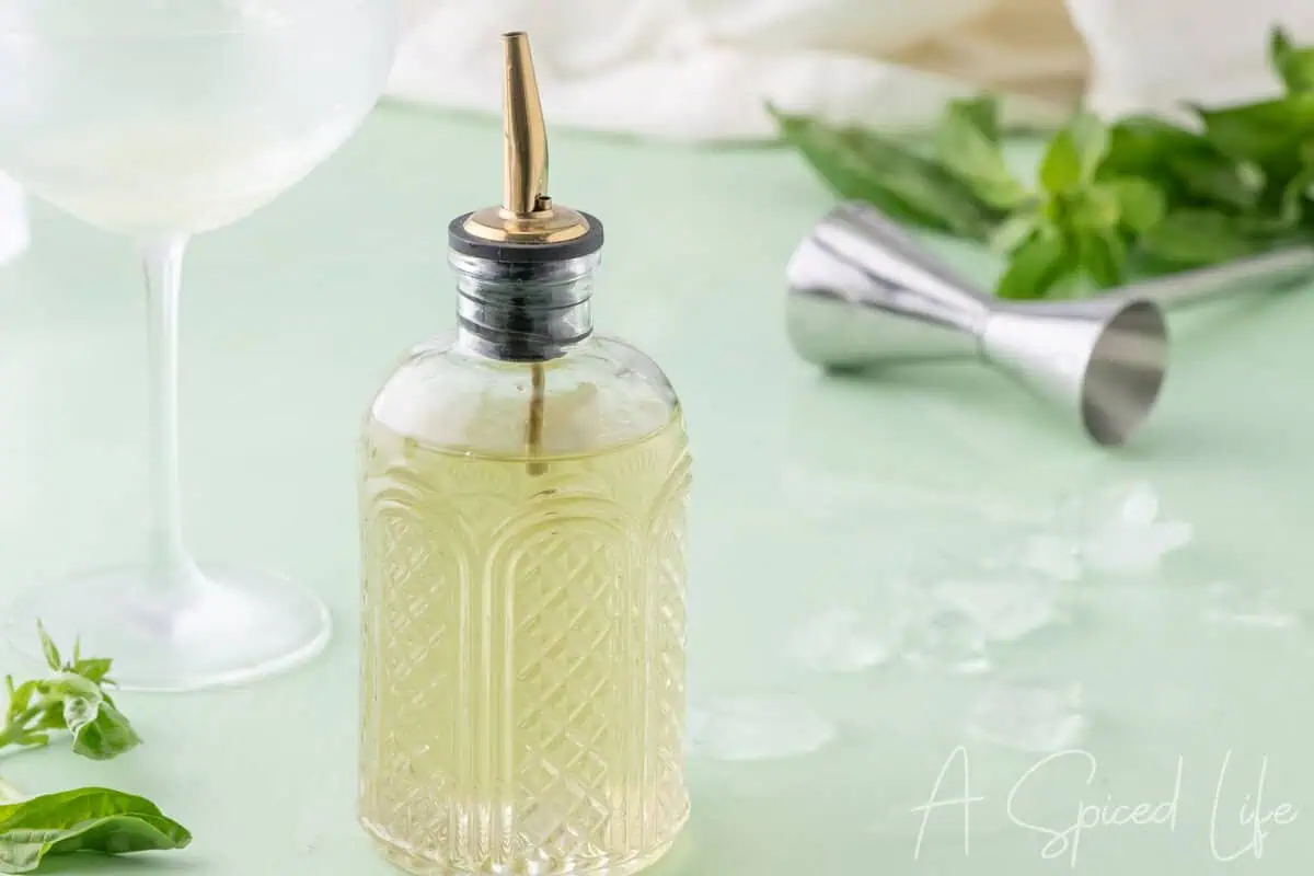 Basil-infused syrup in a glass bottle with cocktail glass, ice, and bar tools