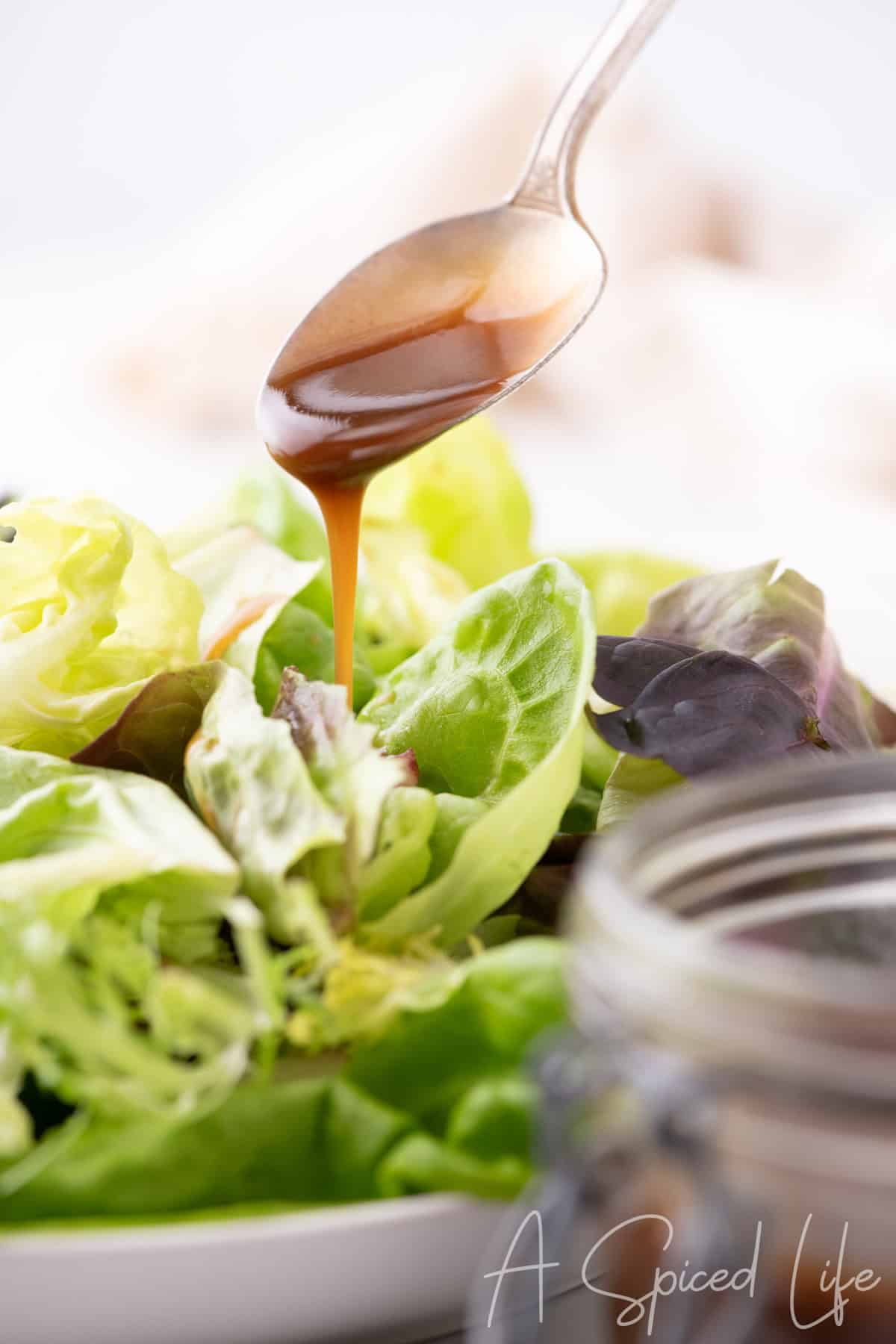 Balsamic dressing being poured from a spoon over mixed salad greens.
