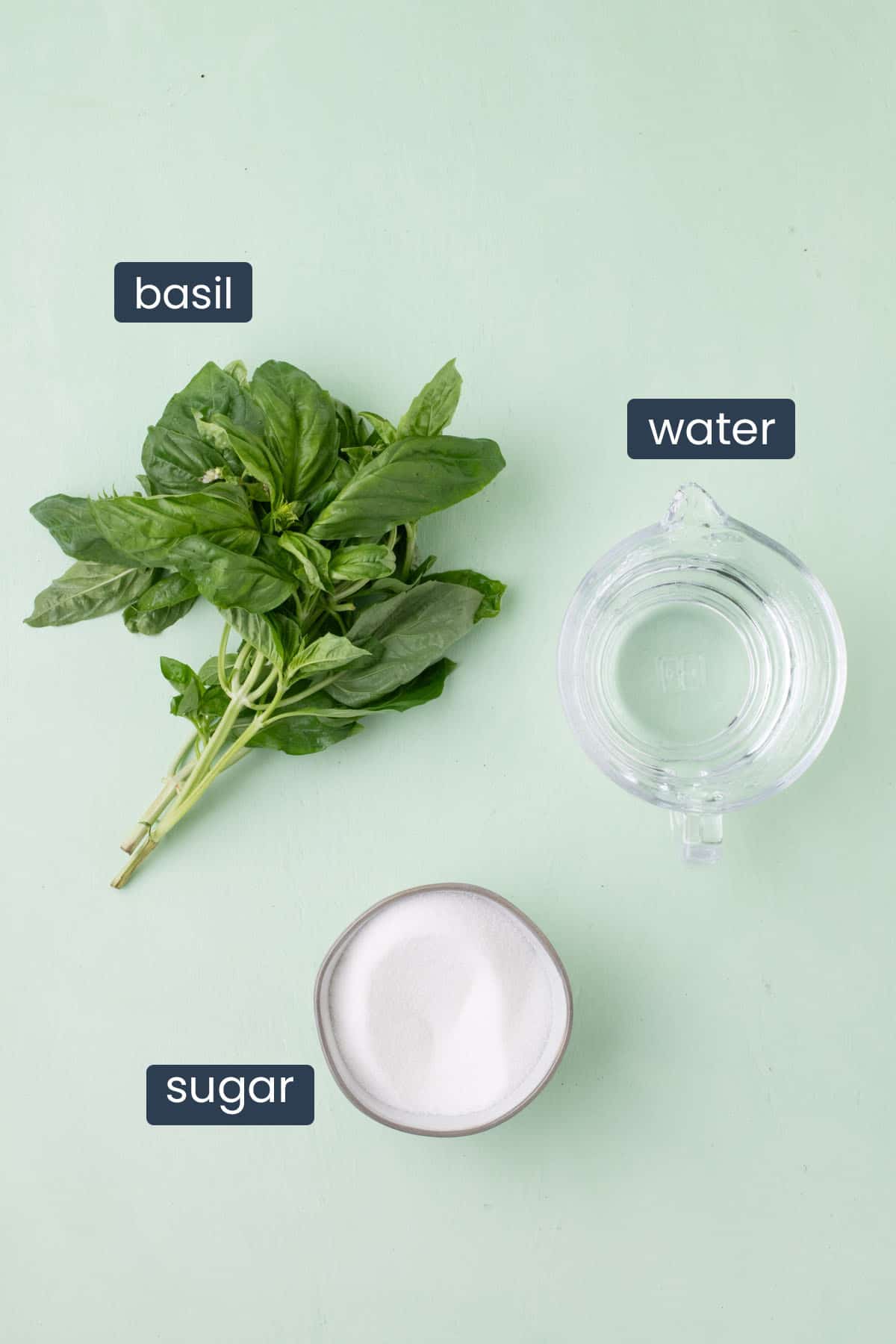 Fresh basil leaves, granulated sugar, and water arranged for making basil simple syrup