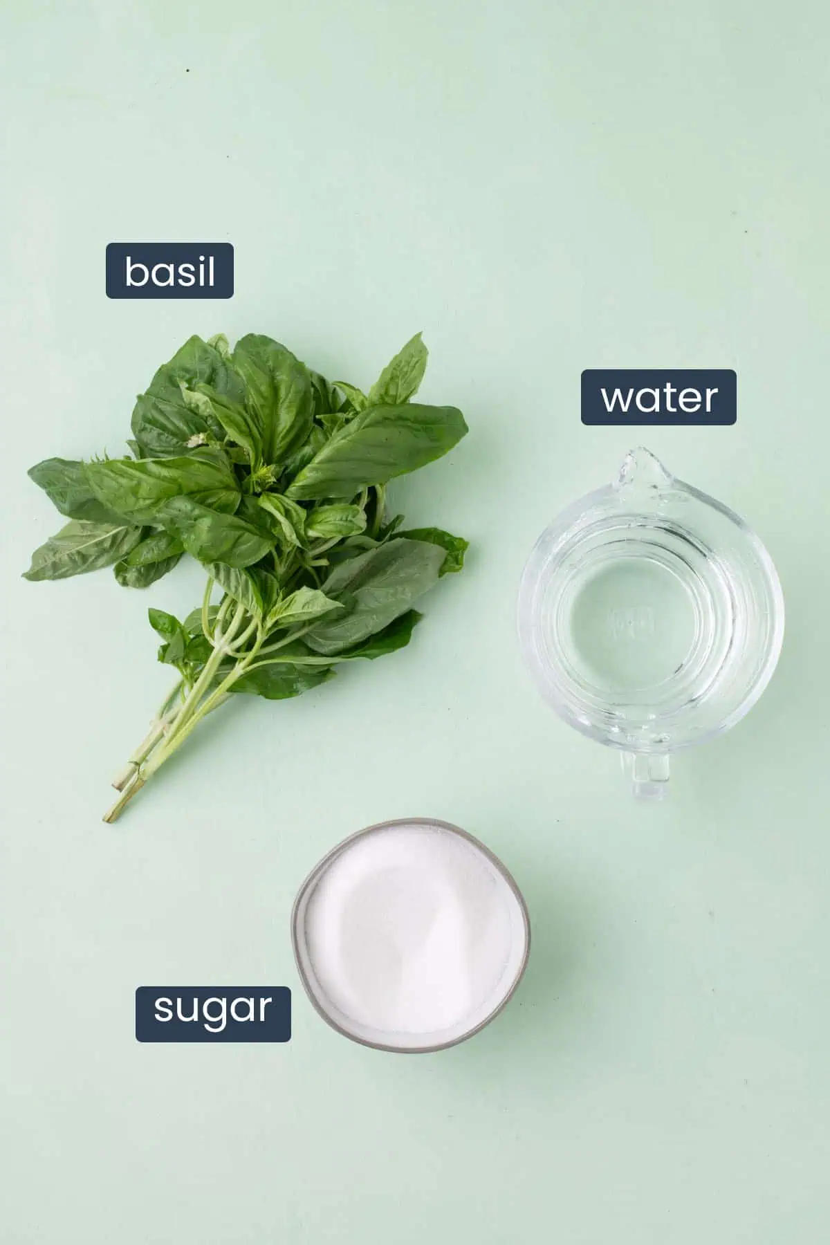 Fresh basil leaves, granulated sugar, and water arranged for making basil simple syrup