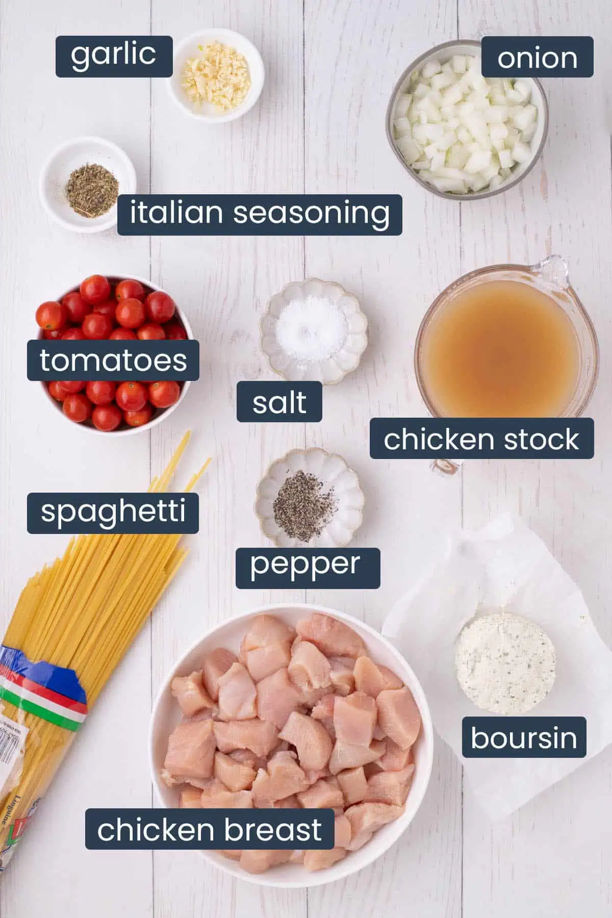 Ingredients for slow cooker chicken spaghetti including chicken breast, spaghetti, garlic, onion, cherry tomatoes, chicken broth, Boursin cheese, and seasonings.