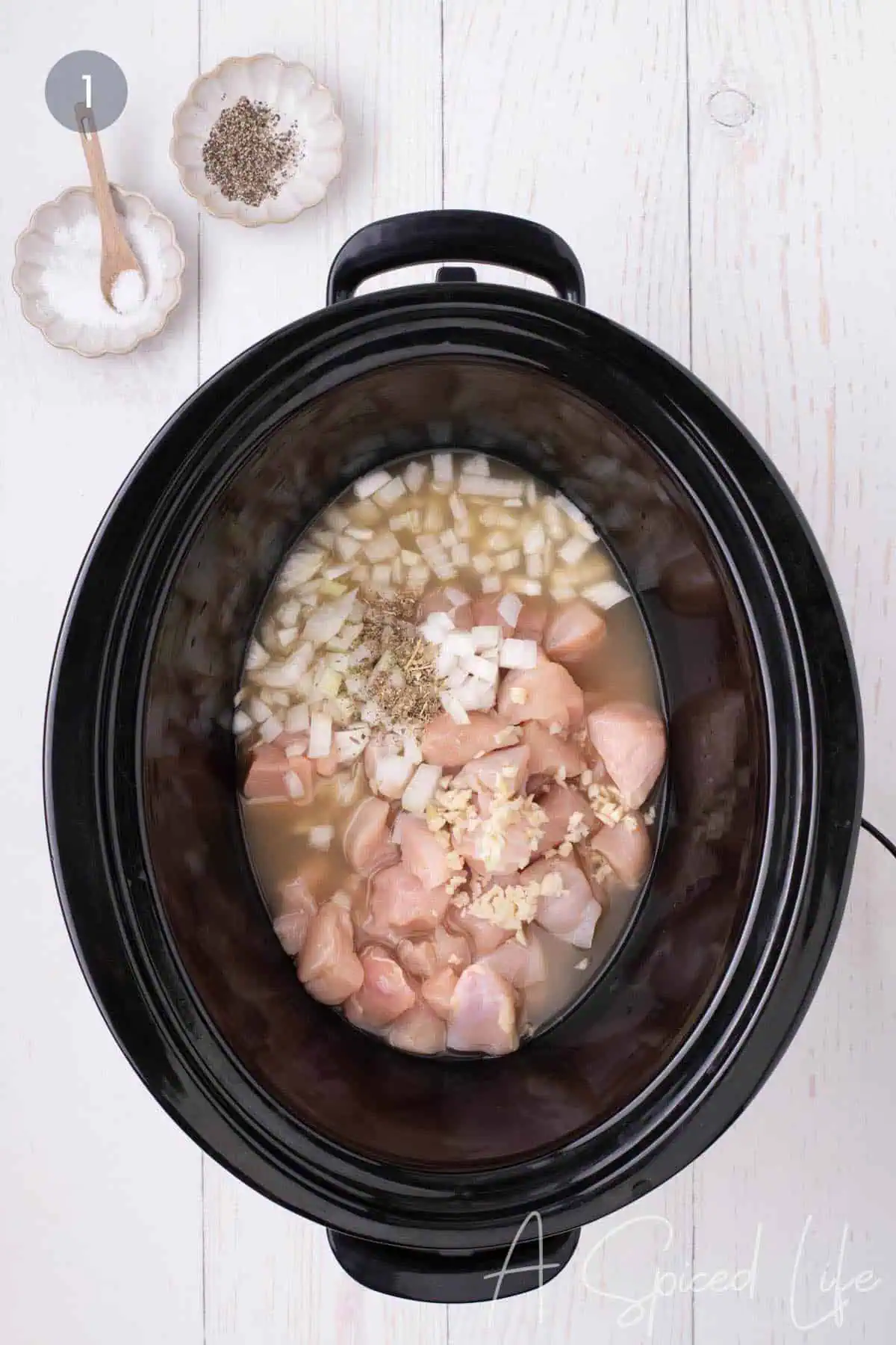Cubed chicken, onion, garlic, broth, and seasonings added to a slow cooker.