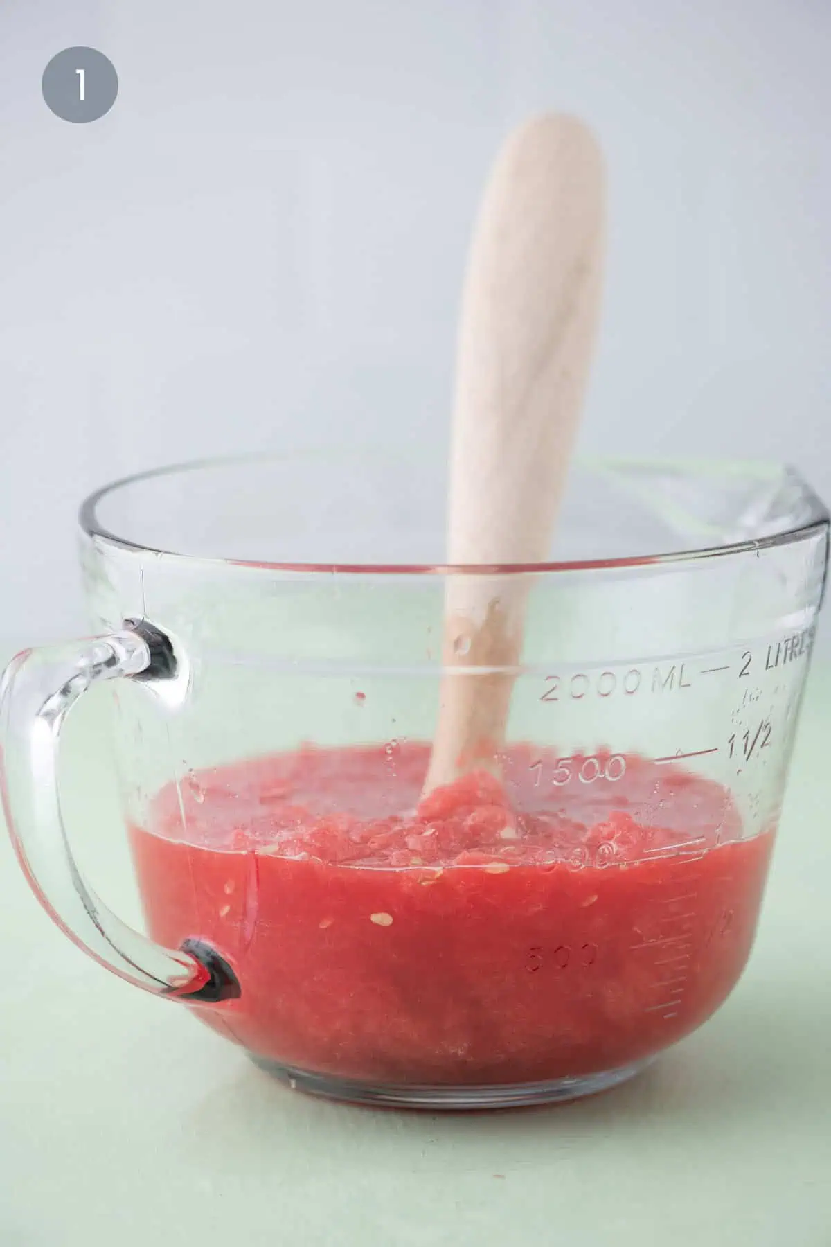 Muddling fresh watermelon in a measuring bowl to release juice
