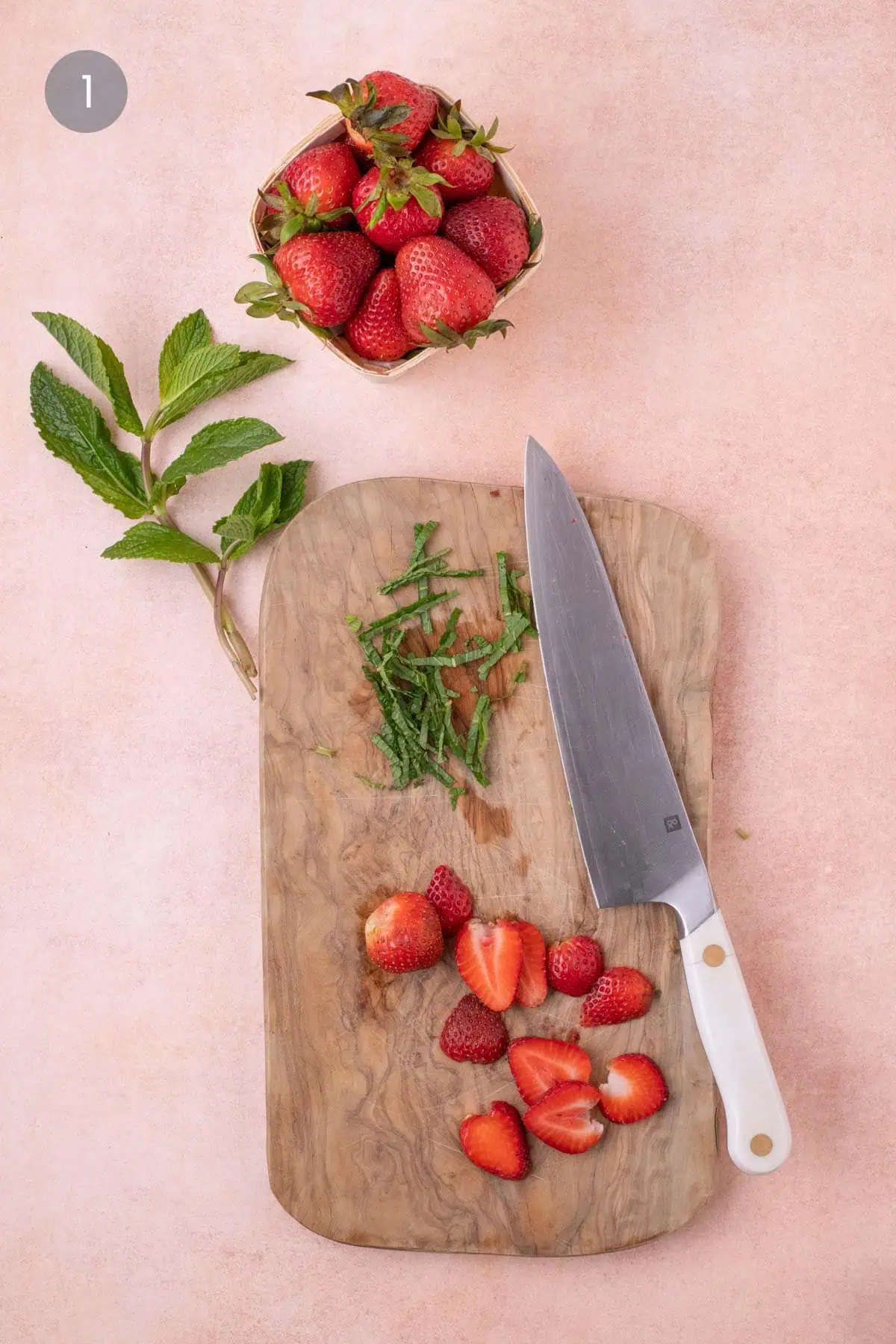 Sliced strawberries and thinly cut mint on a wooden cutting board with knife