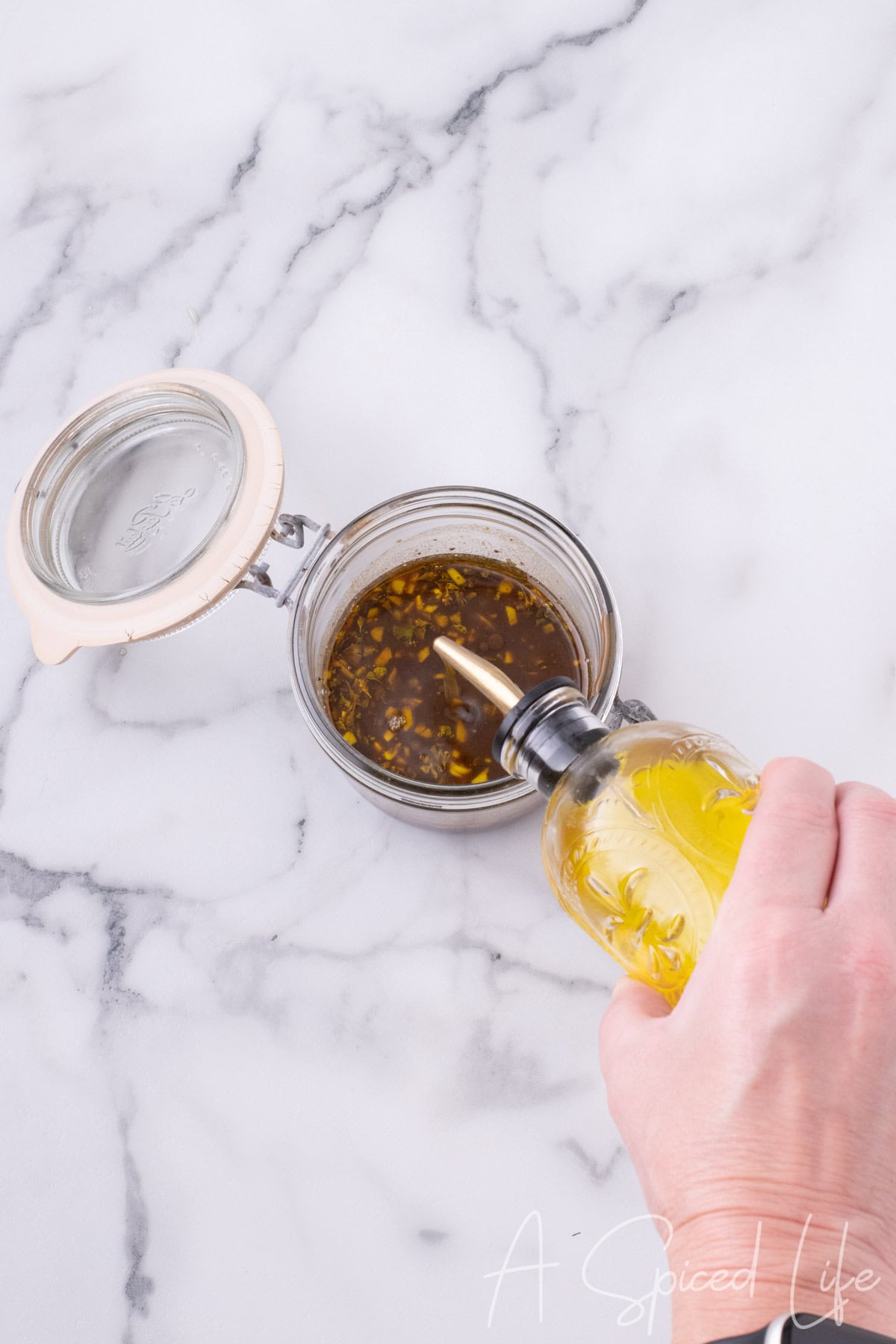 Olive oil being poured into balsamic dressing mixture in a glass jar.