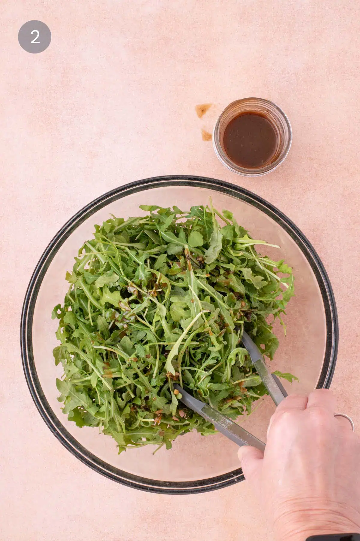 Arugula being tossed with balsamic vinaigrette in a glass mixing bowl