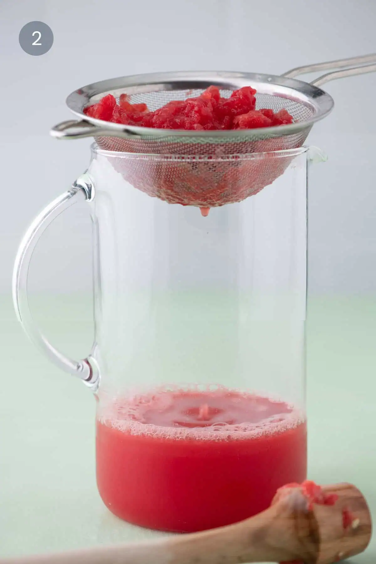 Straining watermelon pulp through a fine mesh sieve into a pitcher