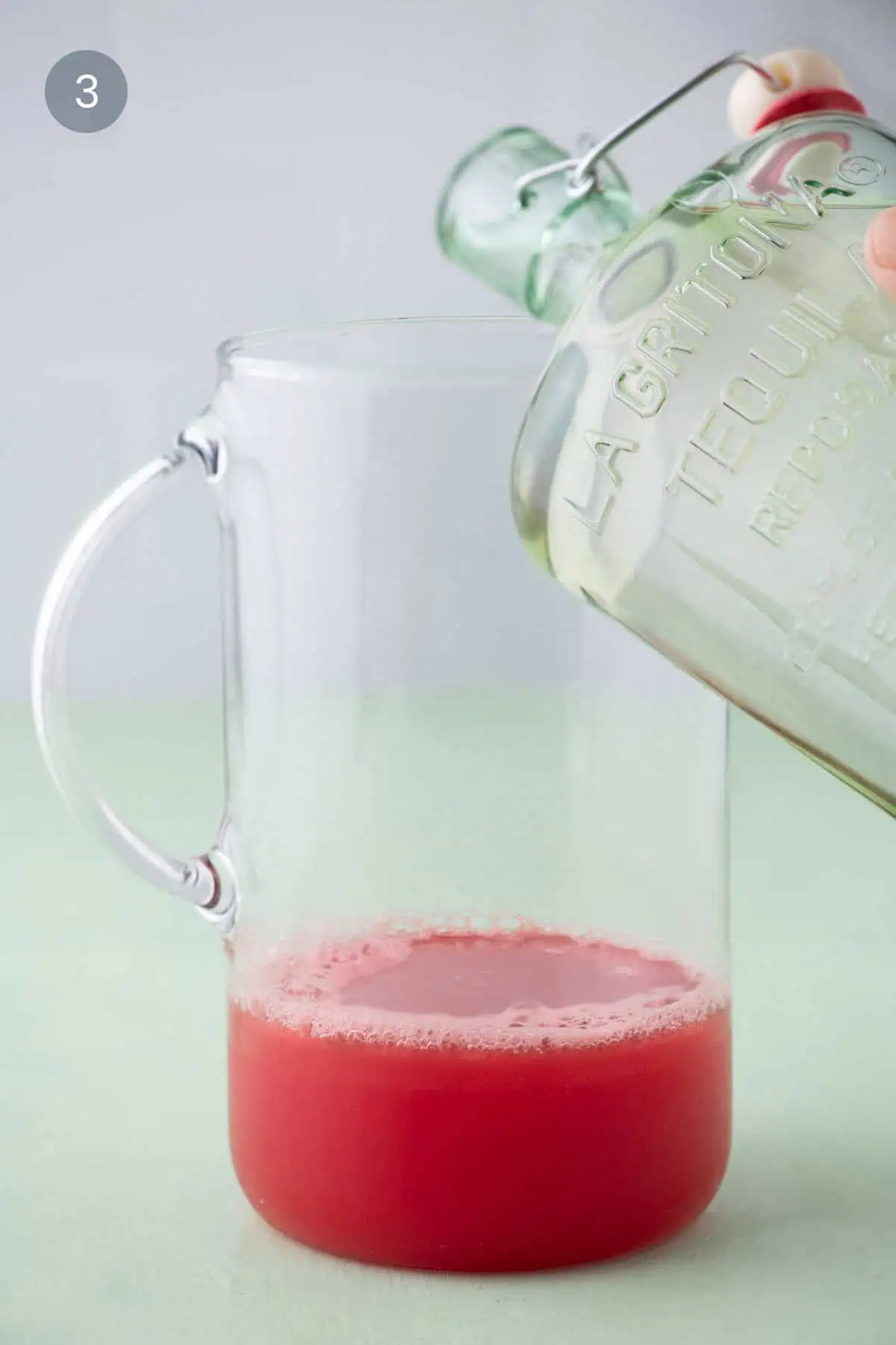 Pouring blanco tequila into fresh watermelon juice in a pitcher