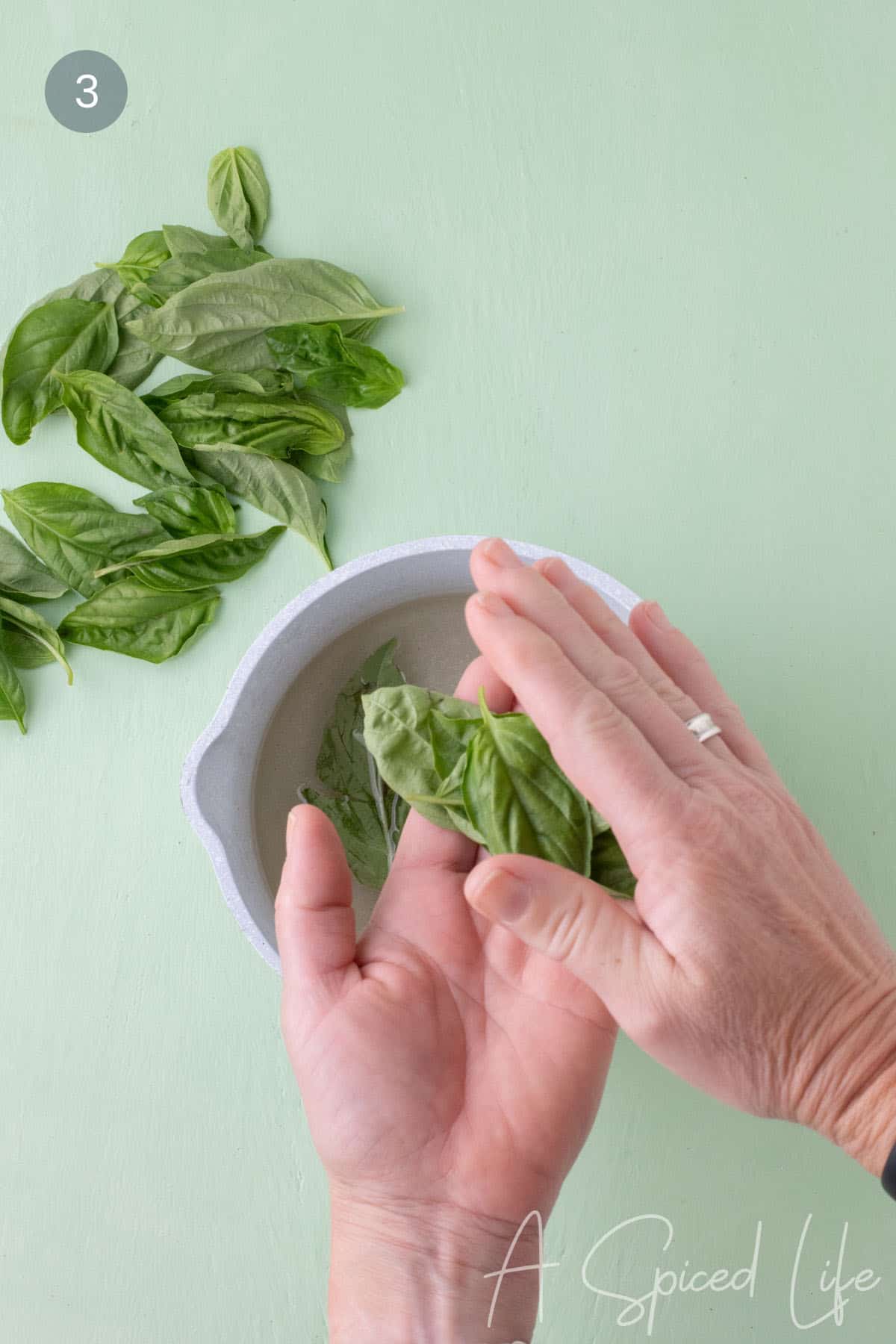 Adding fresh basil leaves to warm simple syrup in a saucepan