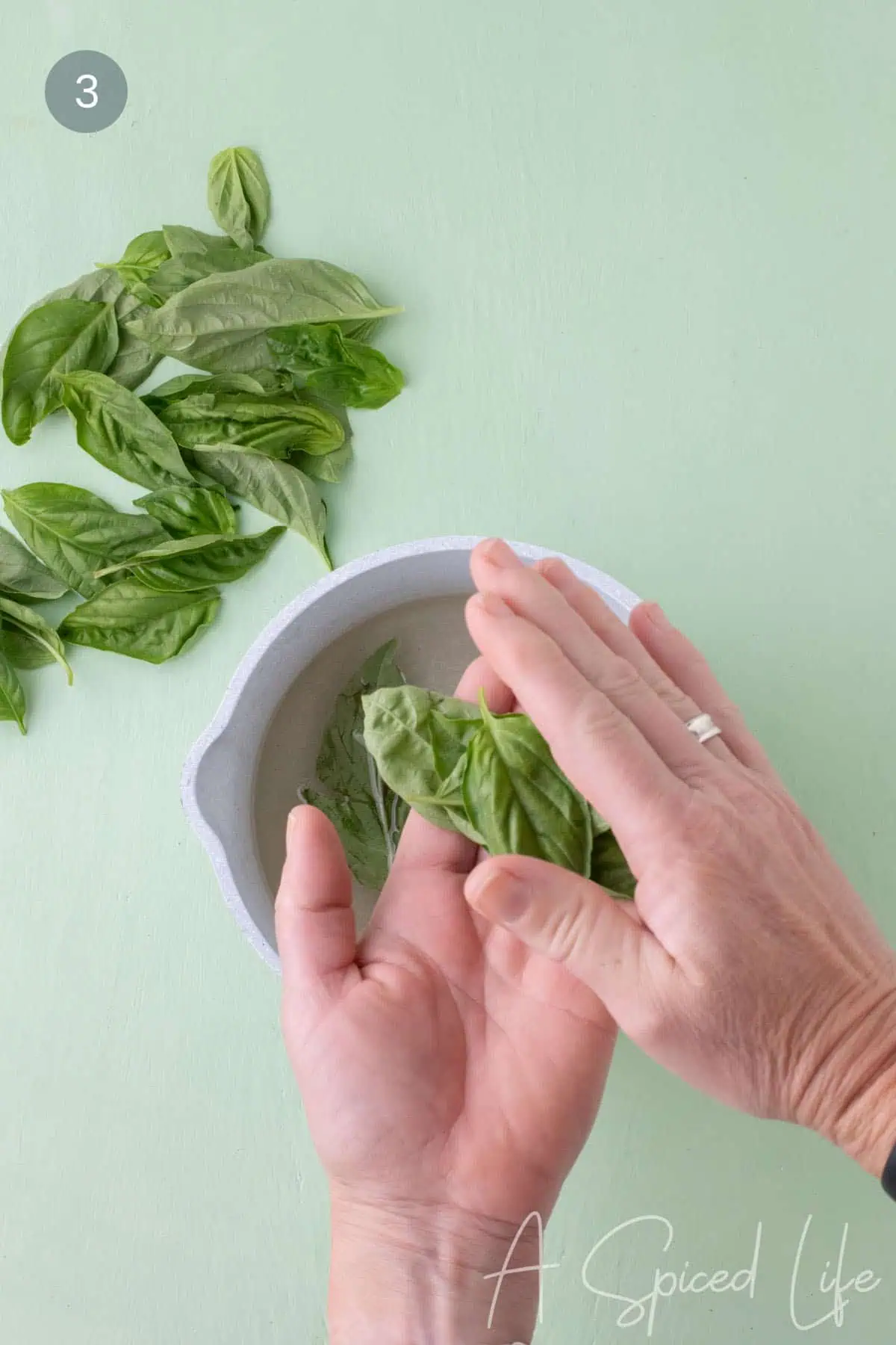 Adding fresh basil leaves to warm simple syrup in a saucepan